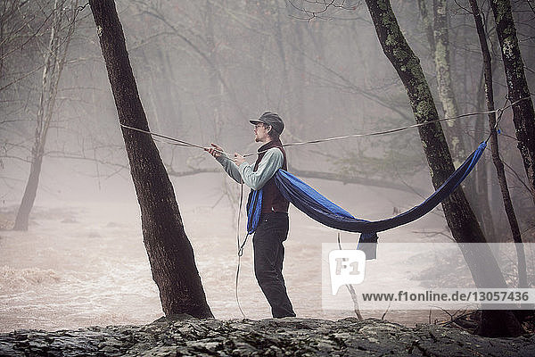 Mann bindet Hängematte an Bäume am Fluss im Wald