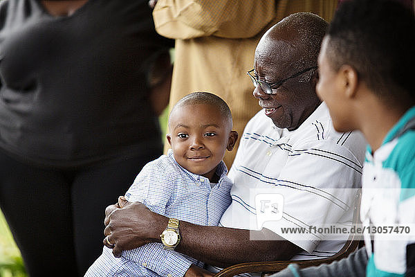Glücklicher älterer Mann umarmt einen Jungen  während er mit seinem Enkel auf der Veranda sitzt