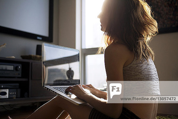 Seitenansicht einer Frau  die einen Laptop-Computer benutzt  während sie zu Hause sitzt
