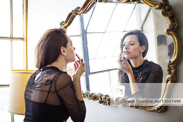 Woman looking at mirror and applying lipstick at home