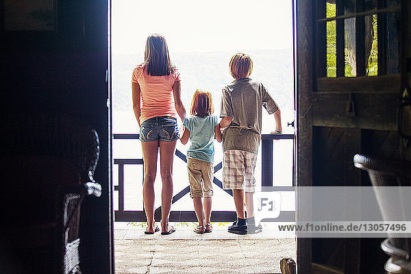 Rückansicht der Geschwister  die auf dem Balkon stehen  durch die Tür gesehen