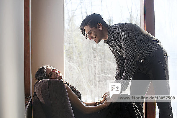 Man holding hands of woman sitting on chair by window at home