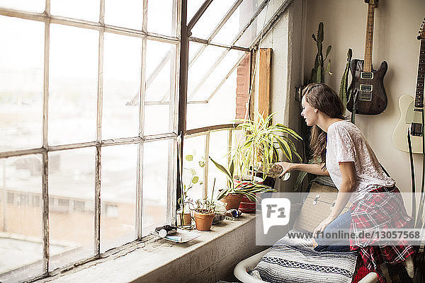 Seitenansicht einer Frau  die zu Hause Topfpflanzen am Fenster gießt