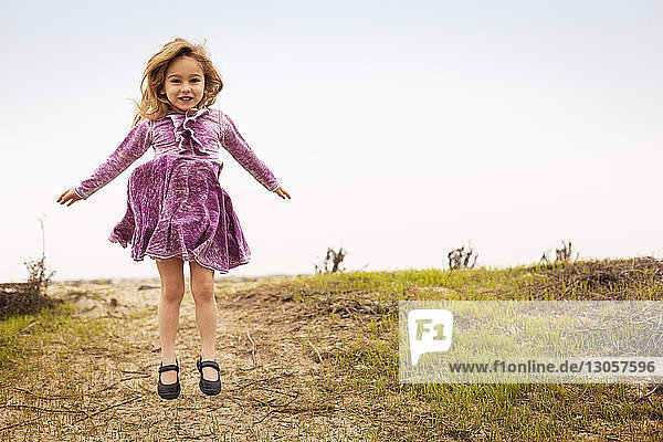 Portrait of cheerful girl jumping on field against sky at beach