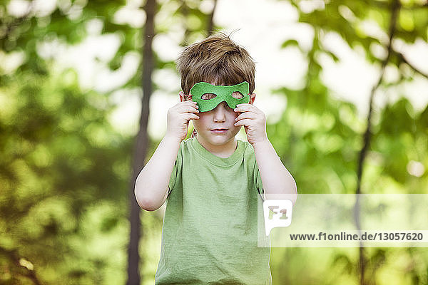 Junge mit Augenmaske  der auf dem Spielplatz an Bäumen steht