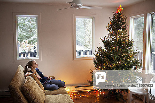 Woman looking at Christmas tree while sitting on sofa