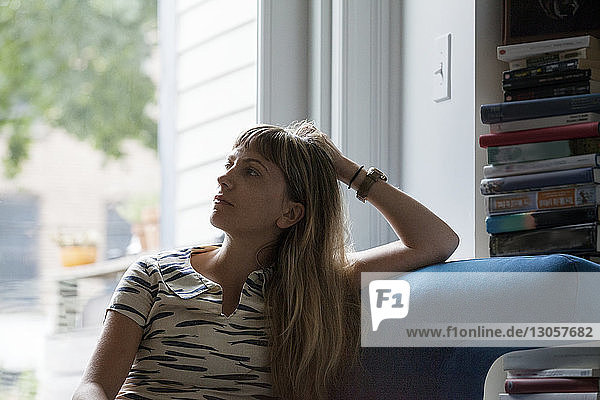 Thoughtful woman sitting on sofa against window at home