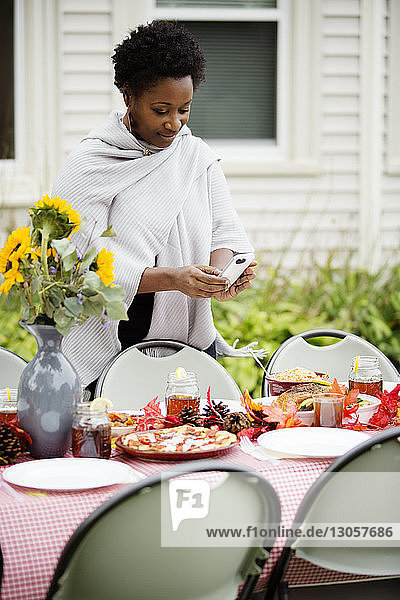 Woman photographing food through phone at table in backyard