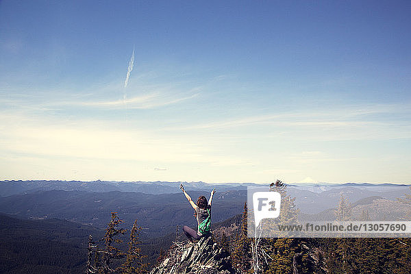 Glückliche Frau sitzt auf einem Felsen und schaut Berge gegen den Himmel