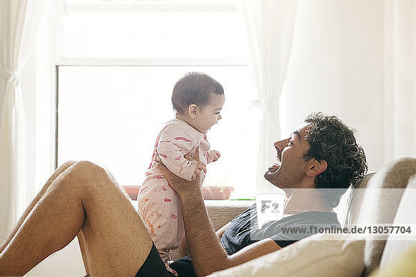 Seitenansicht eines Vaters  der mit seiner Tochter spielt  während er zu Hause auf dem Sofa sitzt
