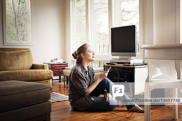 Woman looking away while holding mobile phone at home