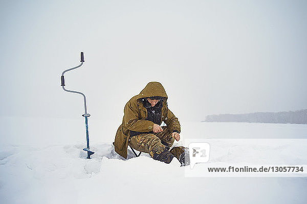 Senior man ice fishing on frozen lake against clear sky