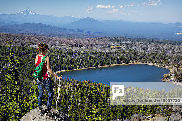 Weibliche Wanderin betrachtet See und Bäume  während sie auf der Spitze einer Klippe steht