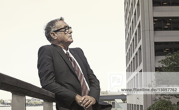 Businessman leaning on railing against sky