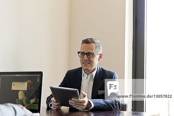 Businessman holding tablet computer while sitting at table in office