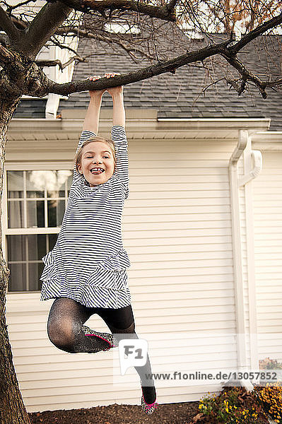 Niedrigwinkelansicht eines fröhlichen Mädchens  das im Hof an einem Baum hängt
