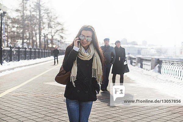 Glückliche Frau telefoniert  während sie auf einem Fußweg geht