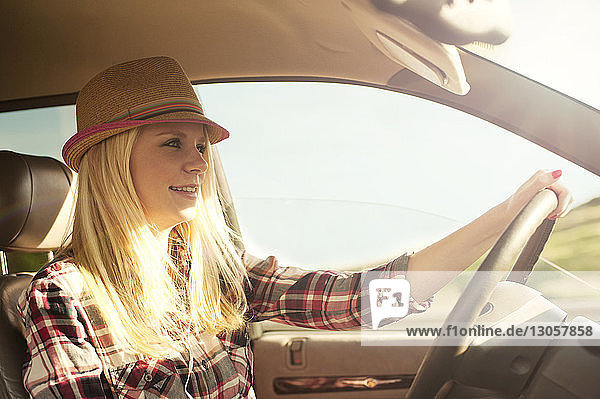 Happy woman in sun hat driving car