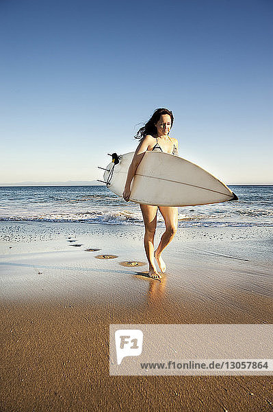 Frau geht am Strand mit Surfbrett am Ufer spazieren