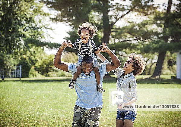 Happy father carrying son on shoulders with daughter at backyard