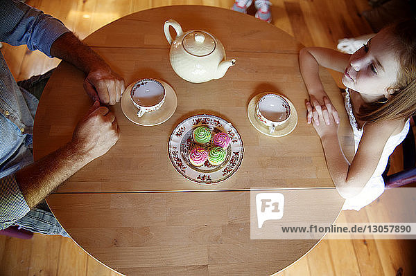 Draufsicht auf Vater und Tochter am Tisch sitzend mit Törtchen und Tee