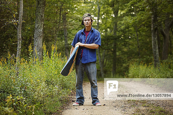 Porträt eines Mannes mit Surfbrett auf einem Feldweg im Wald stehend