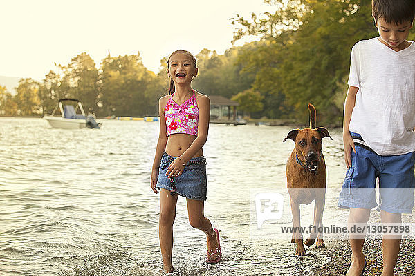 Happy siblings walking with dog at lakeshore