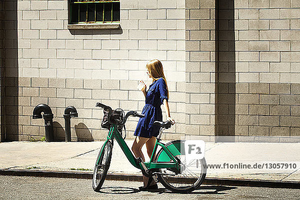 Seitenansicht einer Frau mit Fahrrad  die gegen ein Gebäude in der Stadt steht