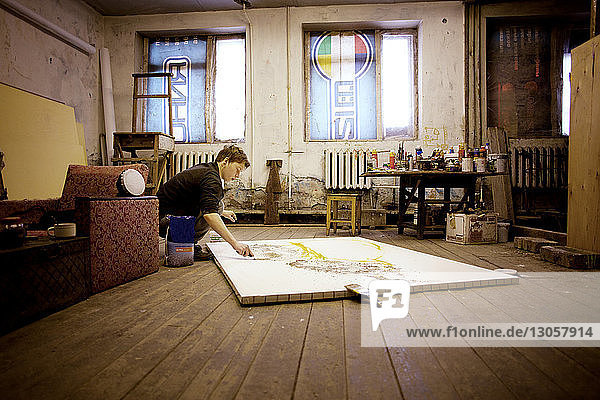Konzentrierter Mann malt in der Hocke beim Workshop