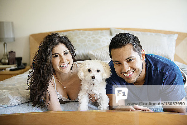 Portrait of happy couple with dog lying on bed at home