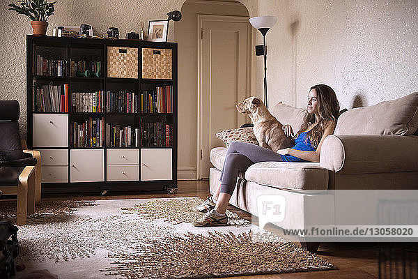 Frau sitzt zu Hause mit Hund auf dem Sofa