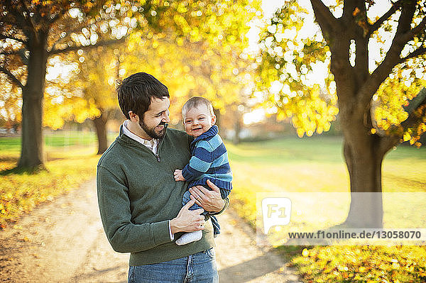 Cheerful father carrying son while standing in park