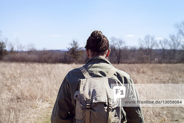 Rear view of male hiker carrying backpack while standing at field during sunny day