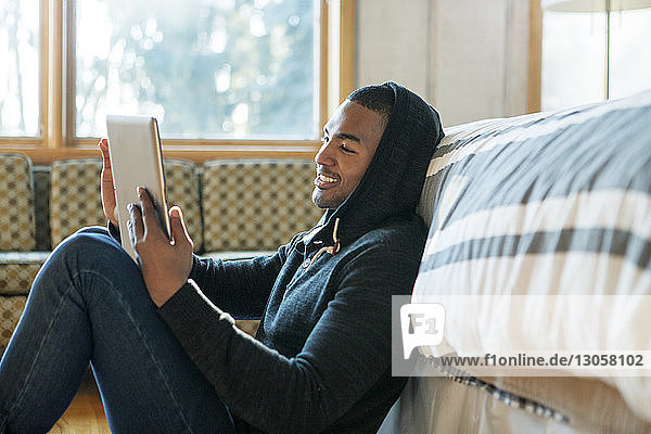 Glücklicher Mann benutzt Tablet-Computer  während er zu Hause am Bett sitzt