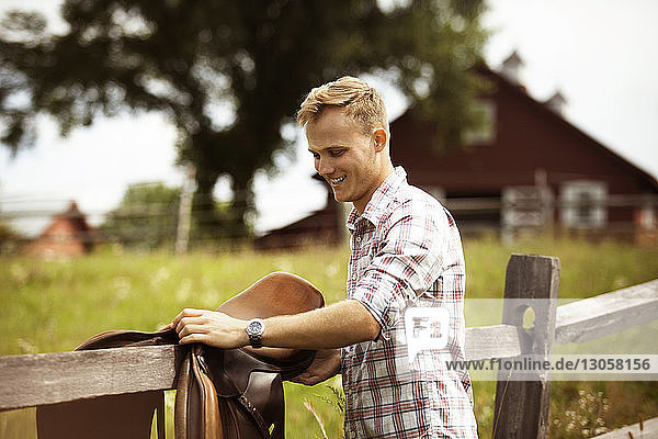 Rancher placing saddle on wooden fence in farm