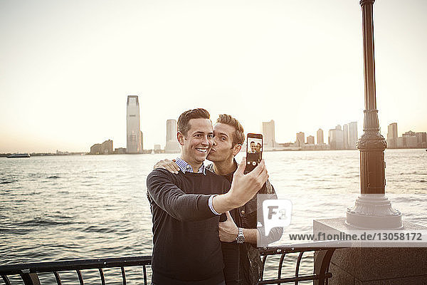 Homosexuelles Paar  das sich am Fluss stehend am Handy selbstständig macht