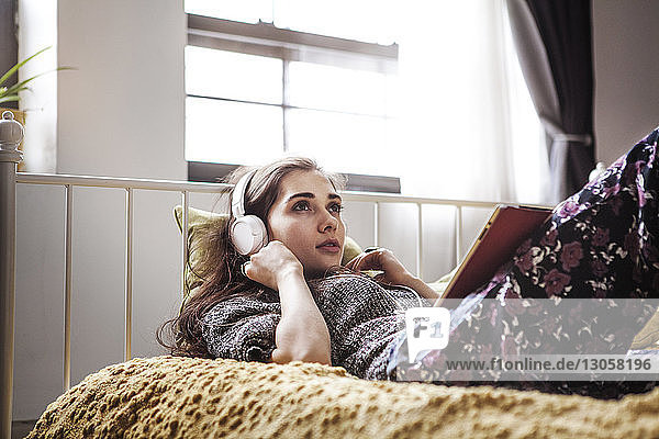 Woman listening to music while lying on bed at home