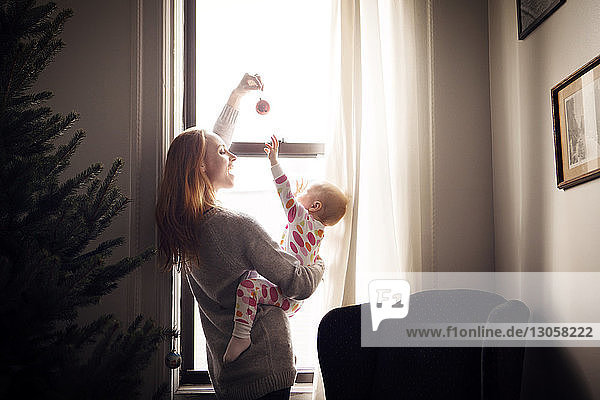 Woman playing with baby girl while standing by window at home