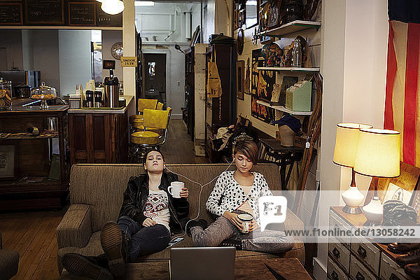 Freunde halten Tassen  während sie im Café auf dem Sofa sitzen