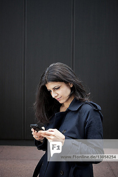 Junge Frau benutzt Smartphone,  während sie an der Wand steht