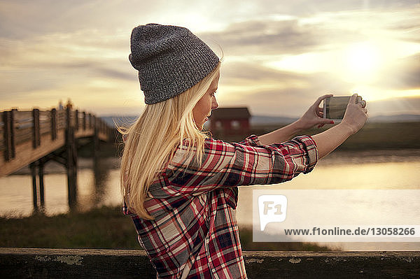 Woman photographing with mobile phone during sunset