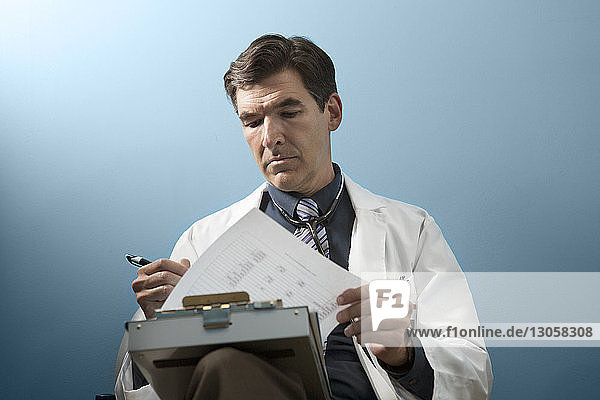Arzt sieht Dokumente an  während er an der Wand sitzt