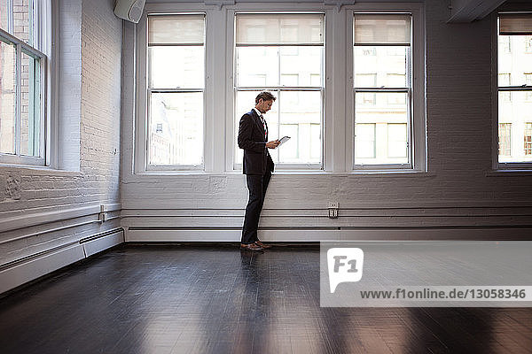 Businessman using tablet while standing by window at office