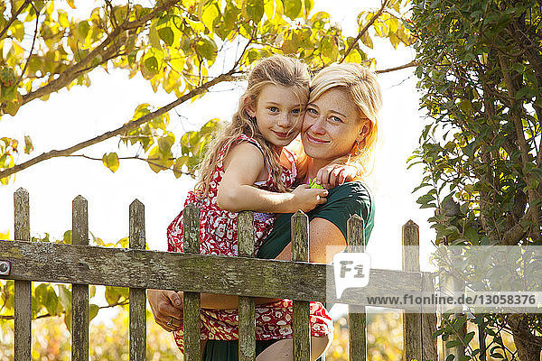 Portrait of mother carrying daughter by fence