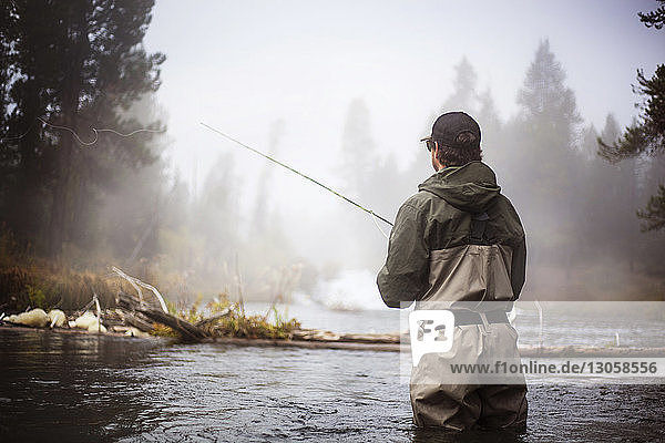 Rear view of hiker fishing in lake during foggy weather