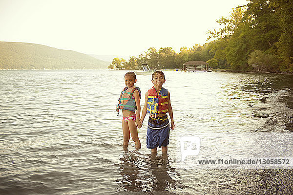 Portrait of siblings wearing life jackets while standing in lake
