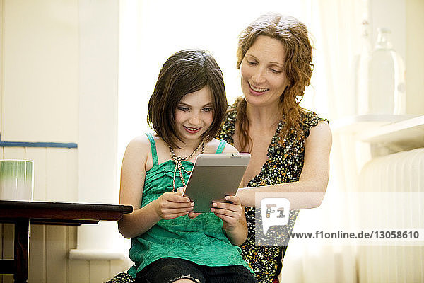Mädchen benutzt Tablet-Computer  während sie mit der Mutter zu Hause sitzt