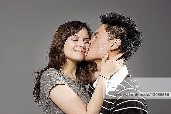Mann küsst Frau vor grauem Hintergrund