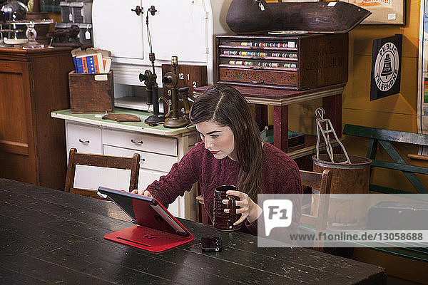 Woman using tablet computer while holding mug at clothing store