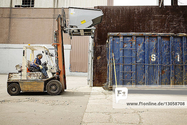 Arbeiter bewegt Container mit Gabelstapler in Recycling-Anlage